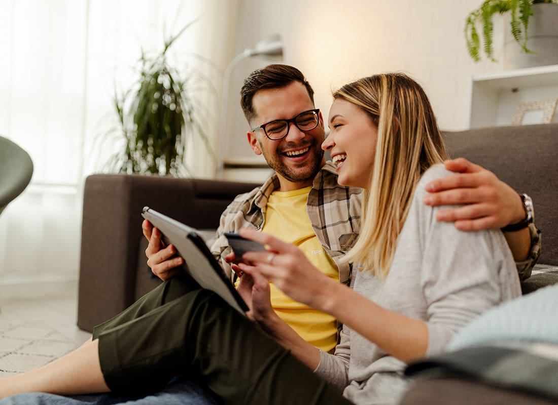 Read Our Reviews - Portrait of a Cheerful Young Married Couple Sitting in the Living Room While Using a Tablet